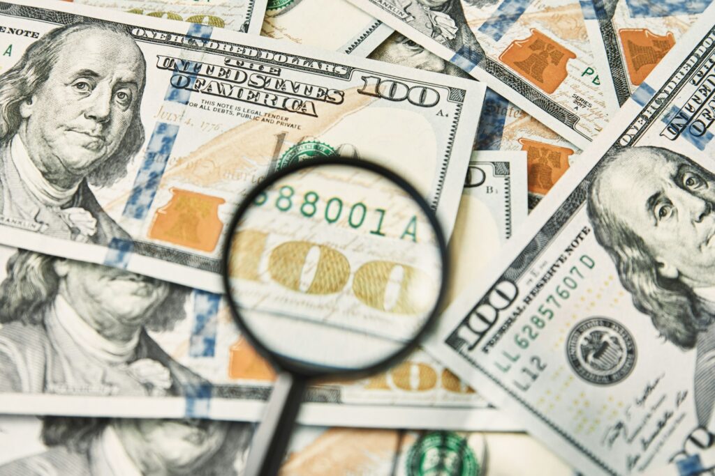 Magnifying glass on a pile of 100 dollar banknotes